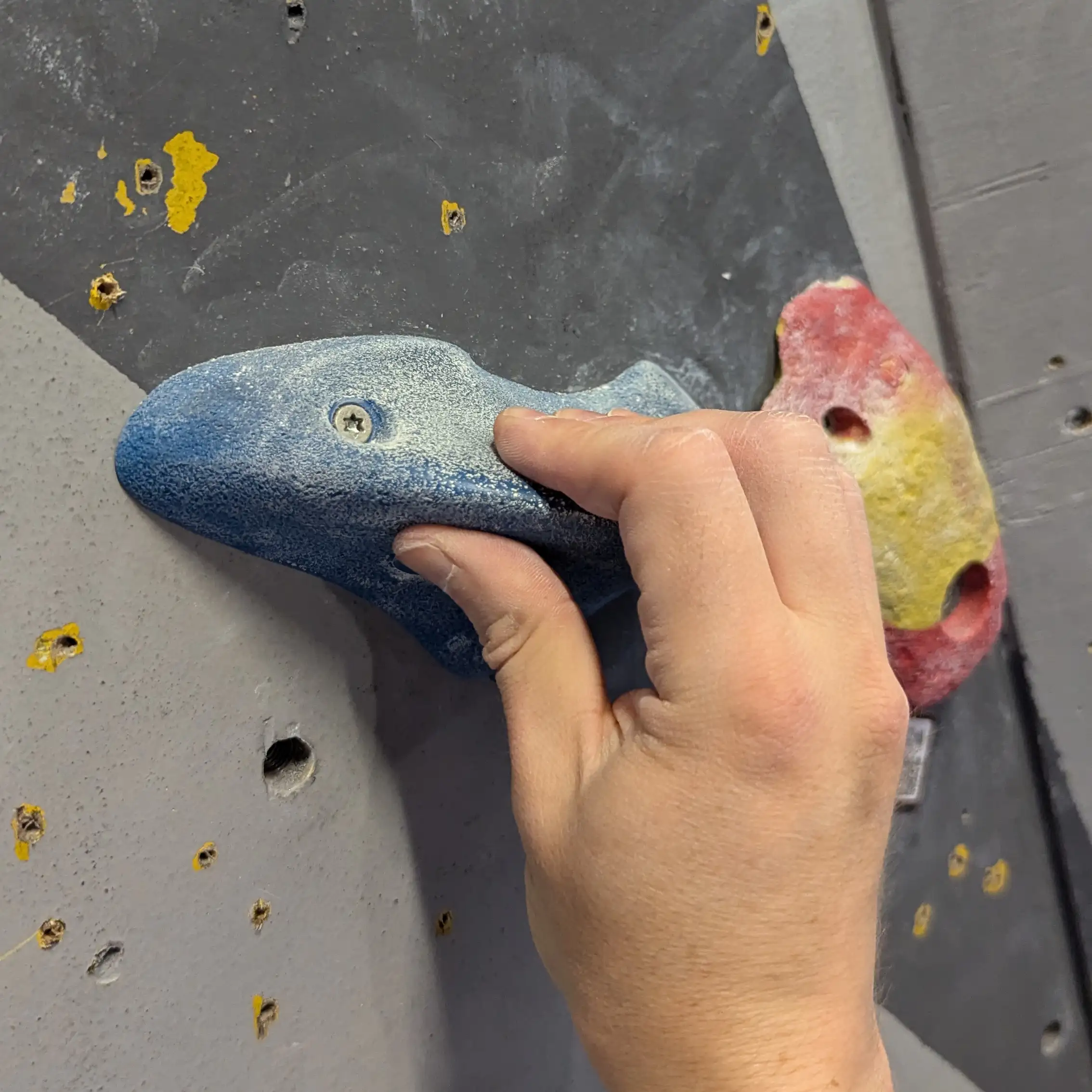 Shows the climber pinching the small blue hold with one hand.