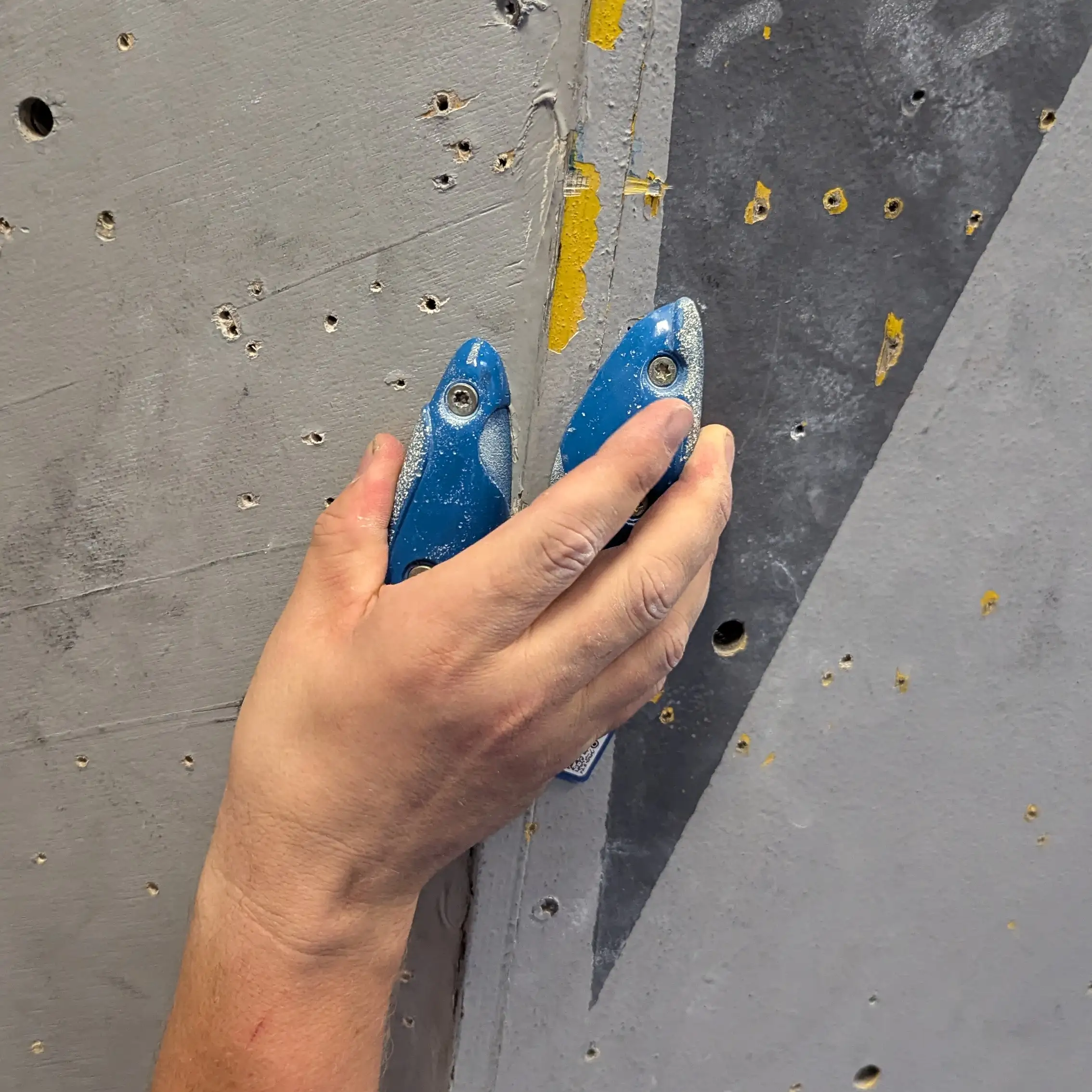 A climber pinching two small holds which are very close to one another. the left hold has the climbers thumb on it and the right hold has his remaining fingers.