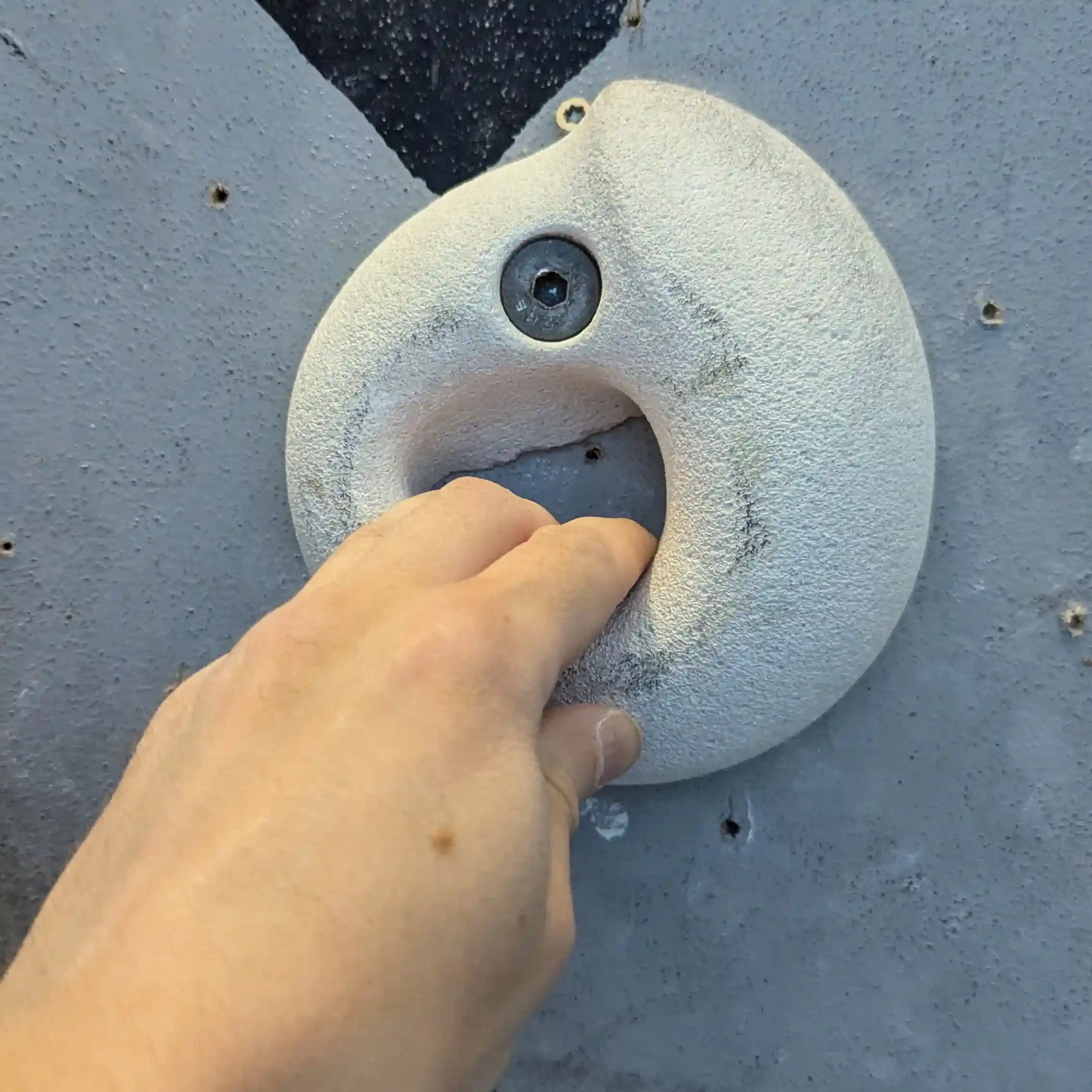 Shows a climber with their 3 fingers placed inside the white sloper hold. Climber is using their thumb for extra grip.