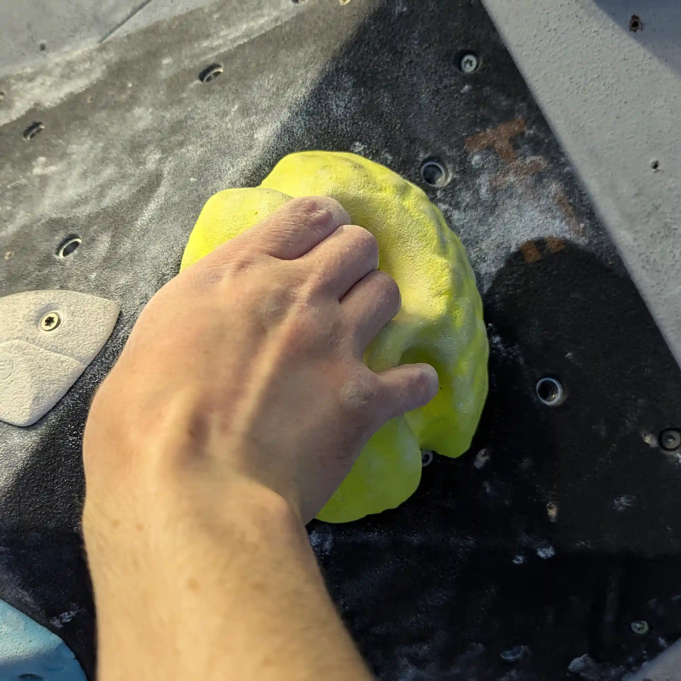 Shows the climber using their hand on the medium yellow pocket hold. They have 3 fingers in the top hole and their pinky finger in the smaller, lower hole.