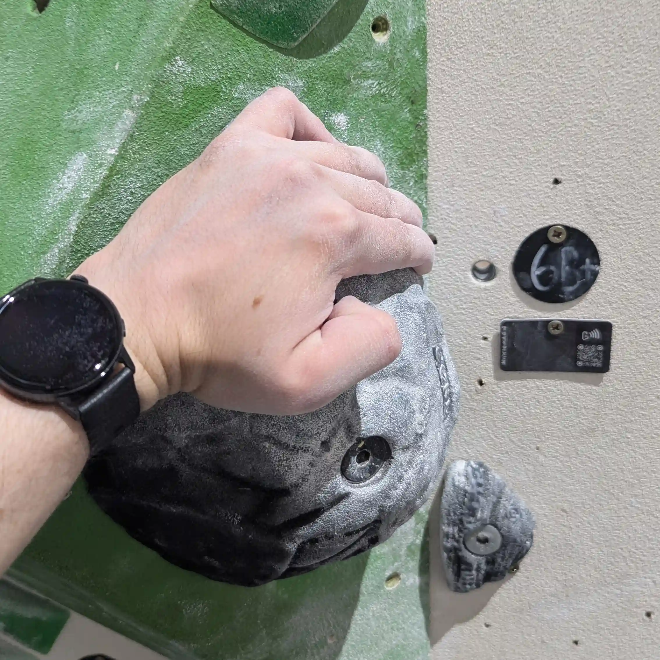 Shows a climber gripping the black, rounded sloper hold with a flat edge in their hand.