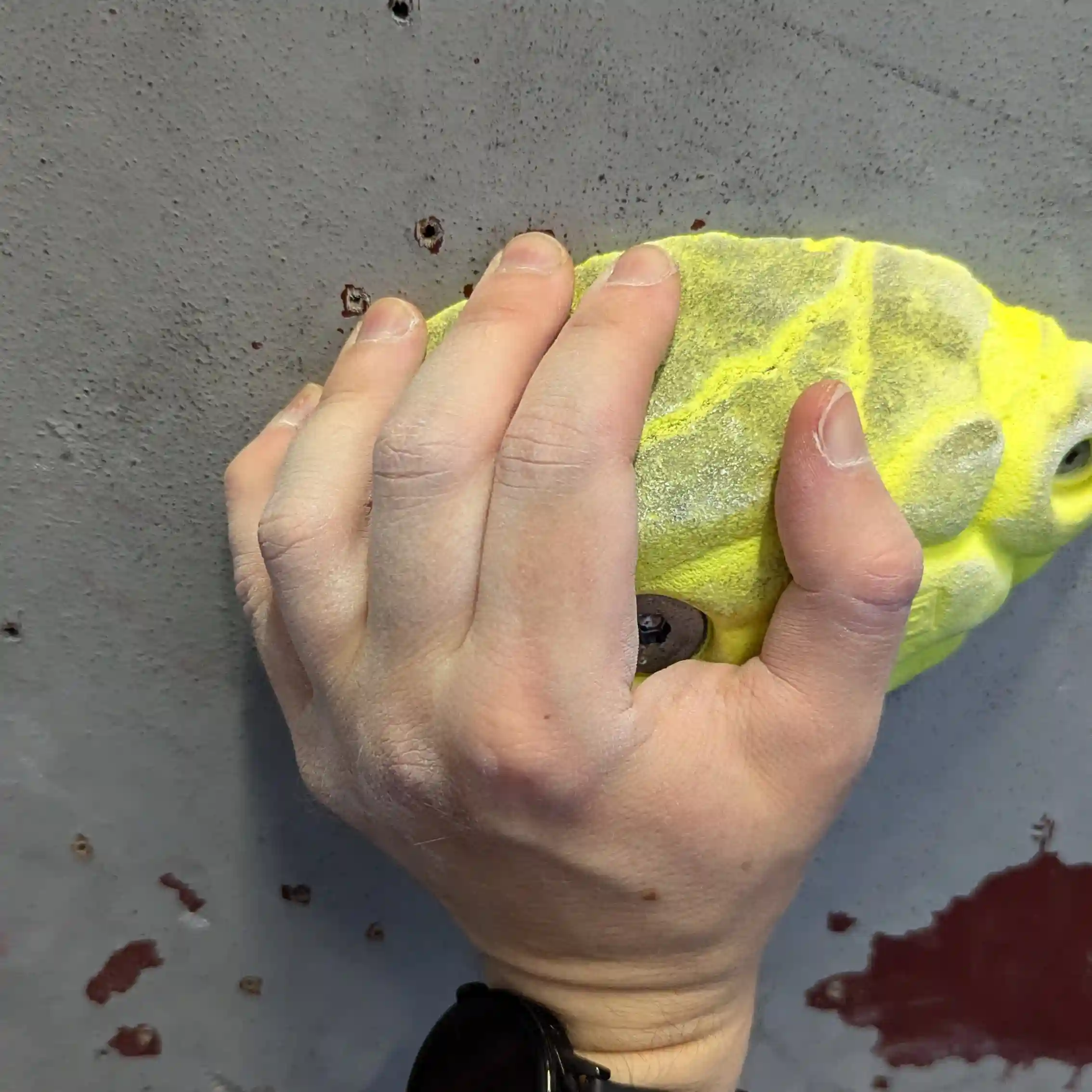 Shows the climber gripping the long, yellow sloper with the pronounced rounded and flat edge. Climber has their fingers tightly placed on the flat edge.