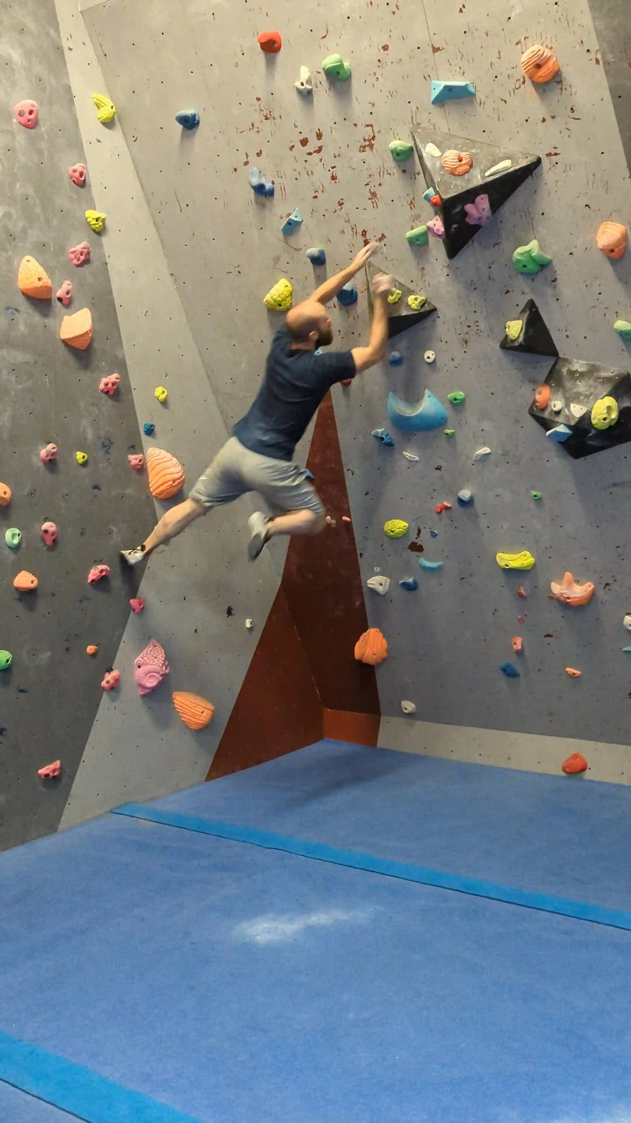 Shows the climber jumping away from the wall and gliding through the air with both arms extended ready to grab onto the holds higher up on another part of the wall.