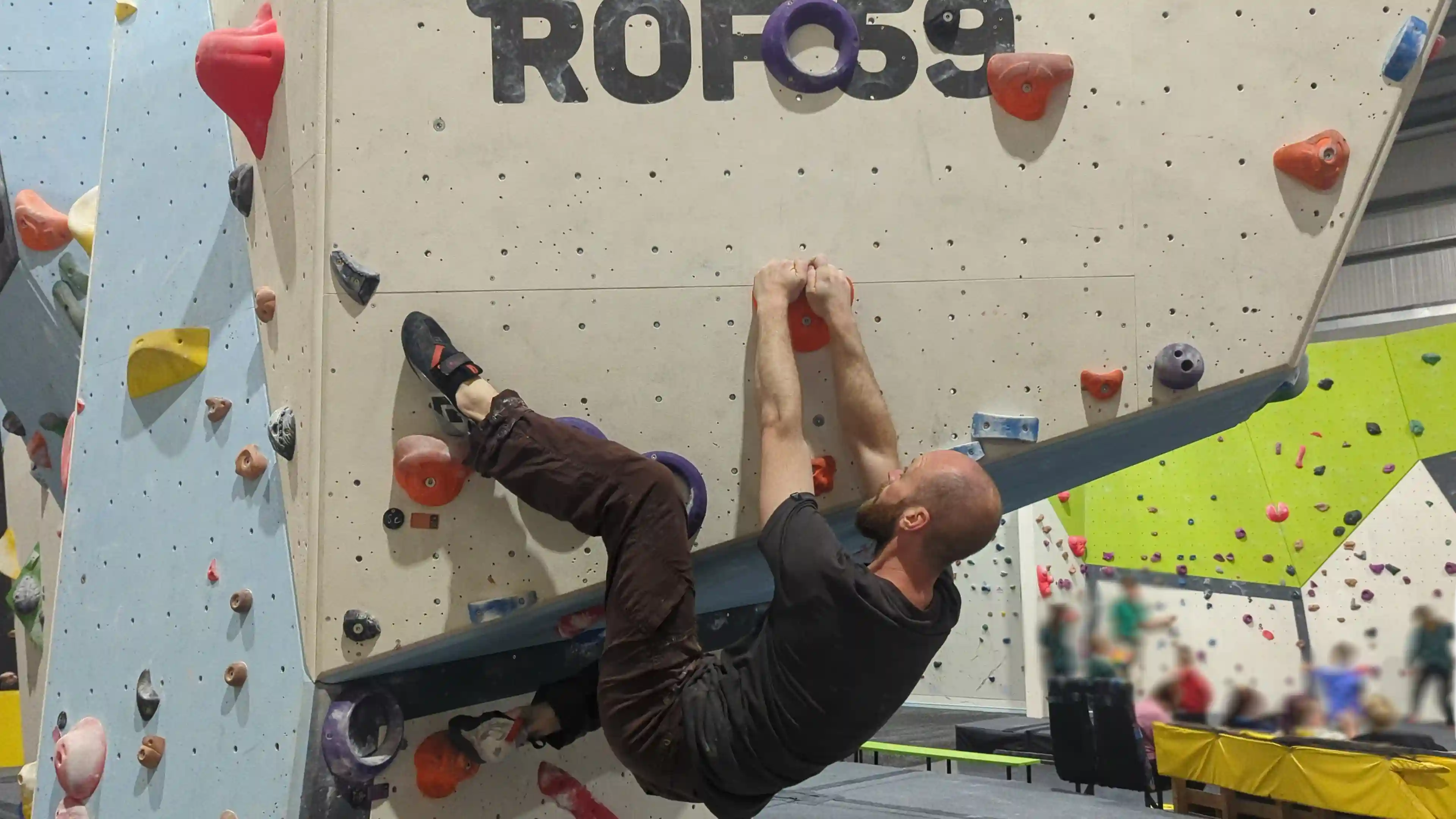 Shows the climber on the bouldering wall hanging horizontally placing their heel on the flat part of the foothold.