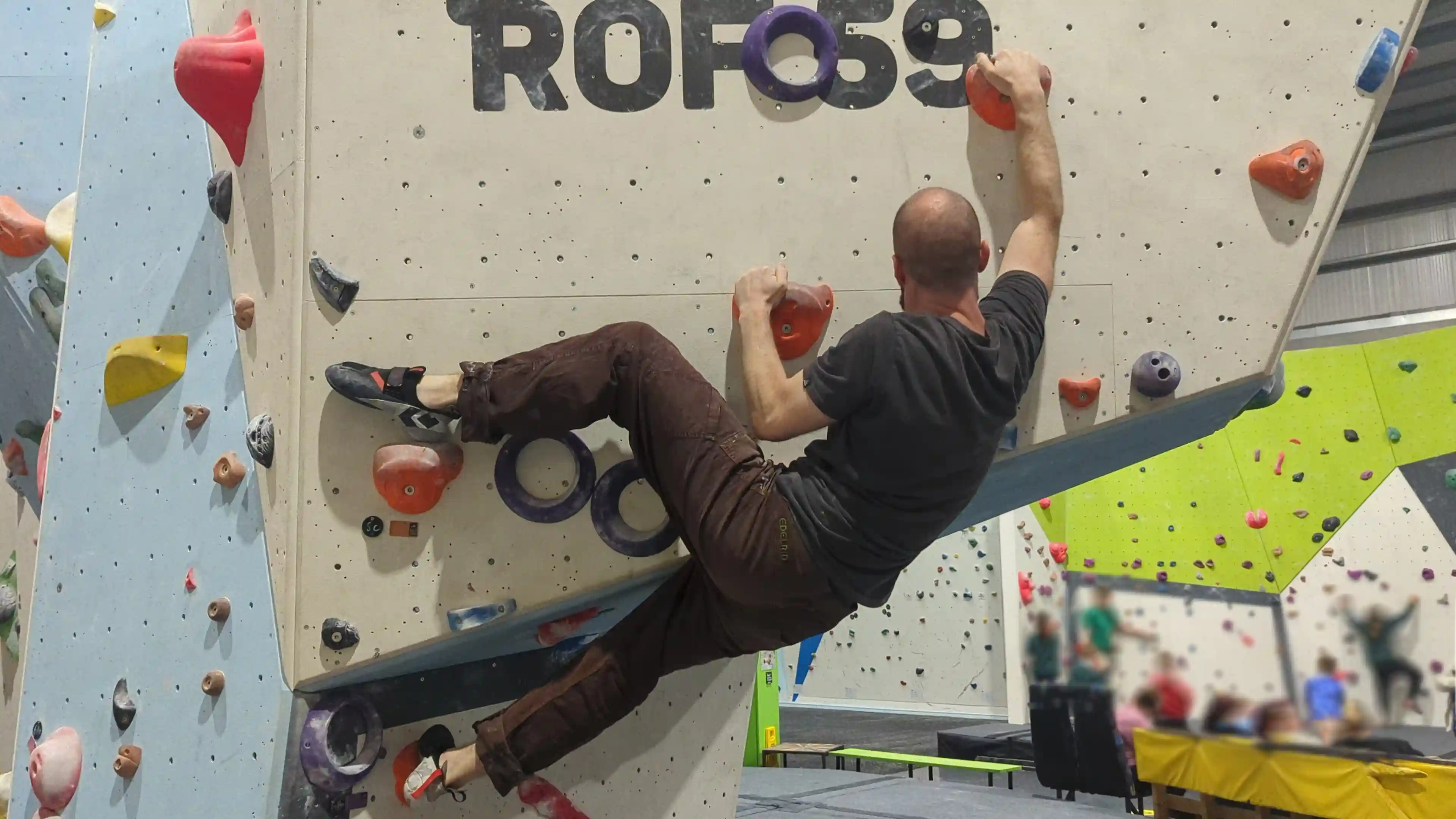 Shows the climber on the bouldering wall with their heel fully tilted over to give them stability and leverage to reach the next hold.