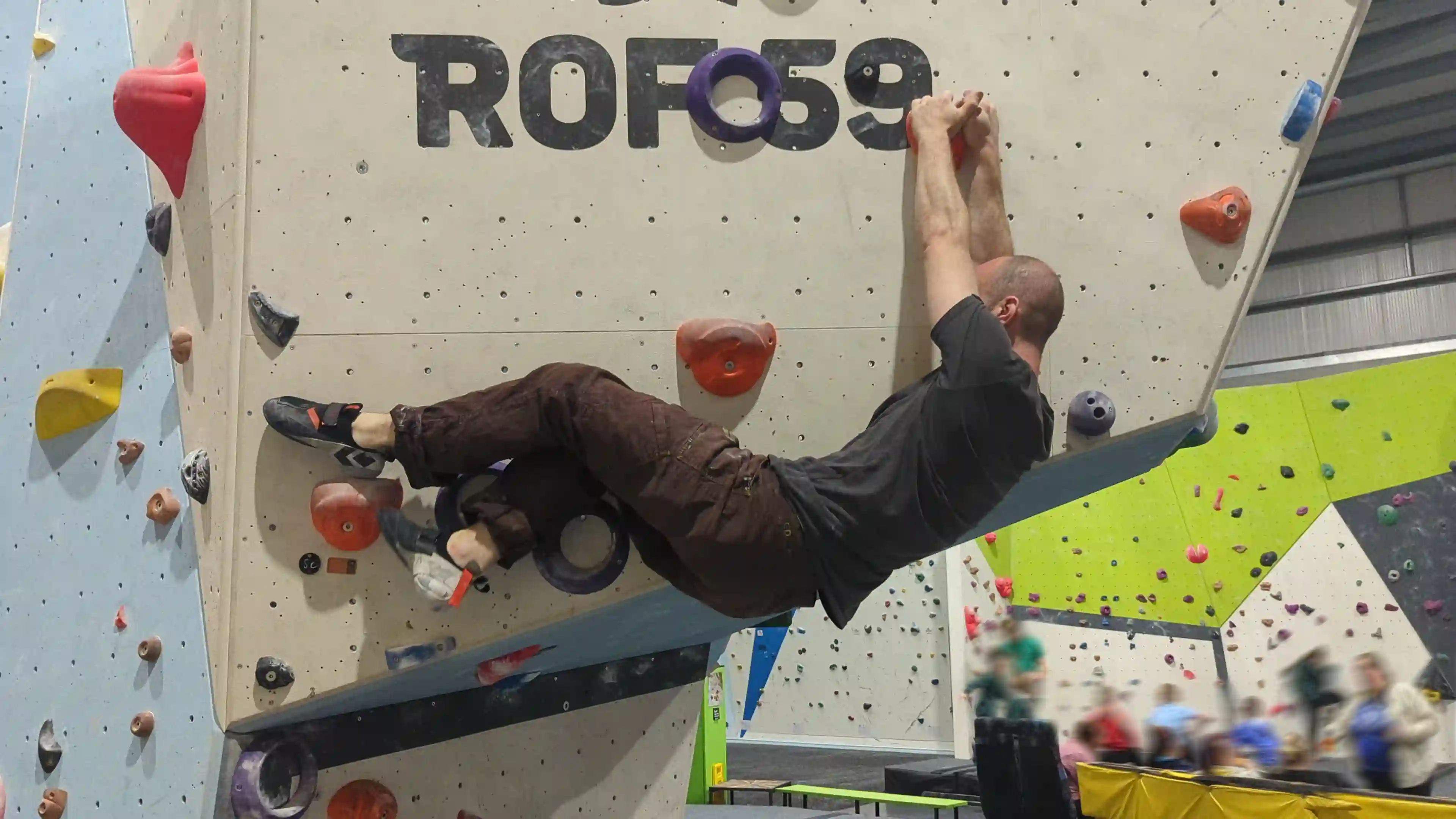 Shows the climber on the bouldering wall advancing to the hold using his opposite foot to swap position on the heel hook hold so that they can use it again for the next foothold.