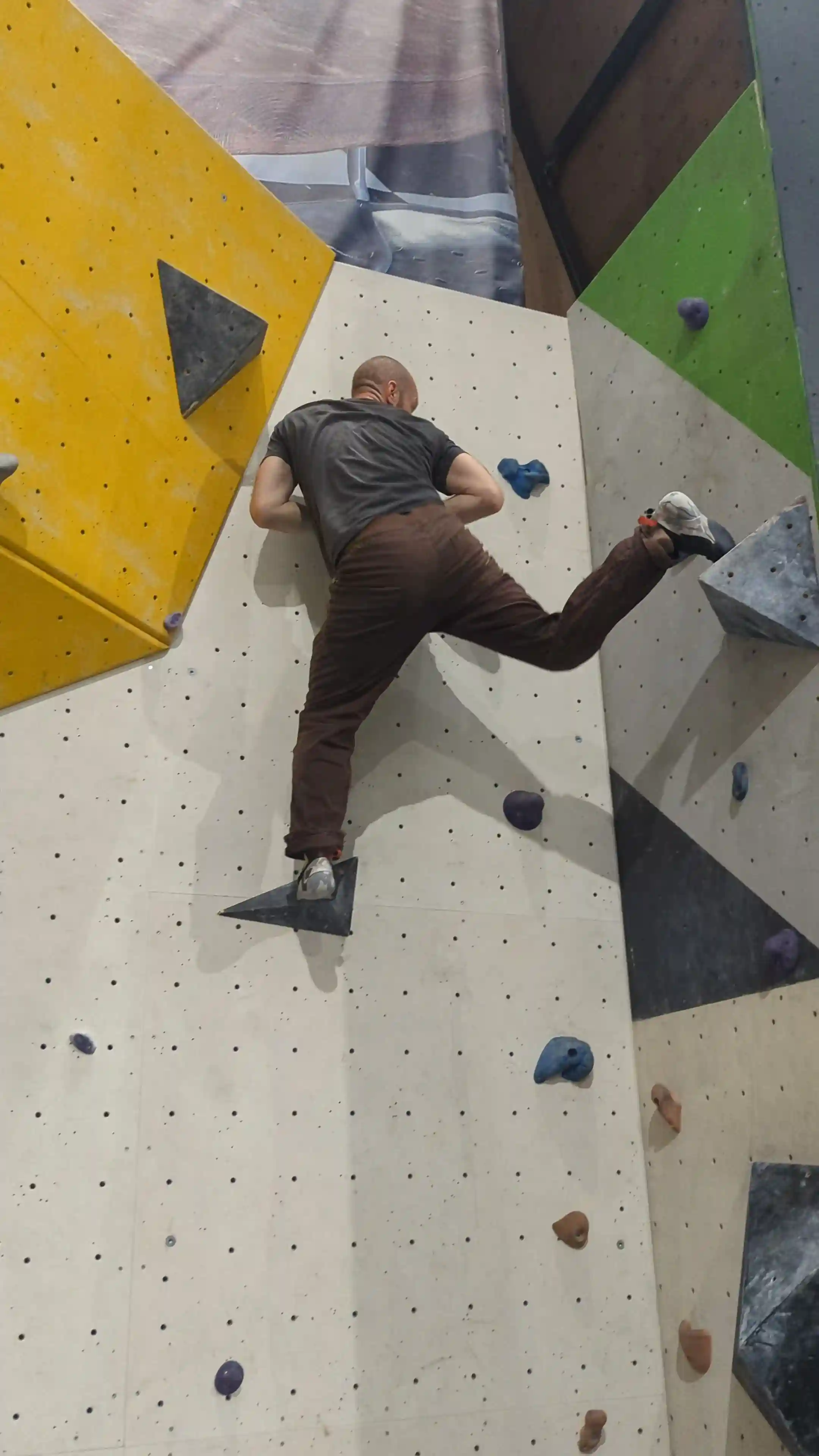 Shows the climber on the bouldering wall performing knee drop technique. The right foot rotates 90 degrees causing the knee to drop down.