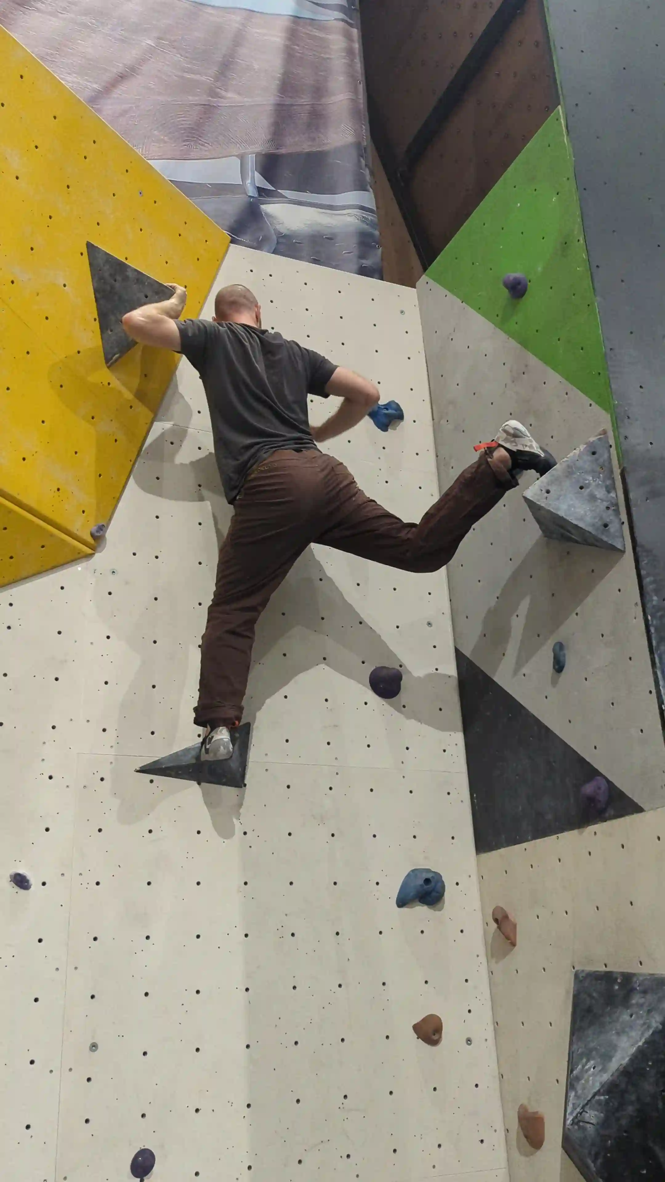 Shows the climber on the bouldering wall after performing knee drop technique. Climber is now facing the correct direction to reach final hold.