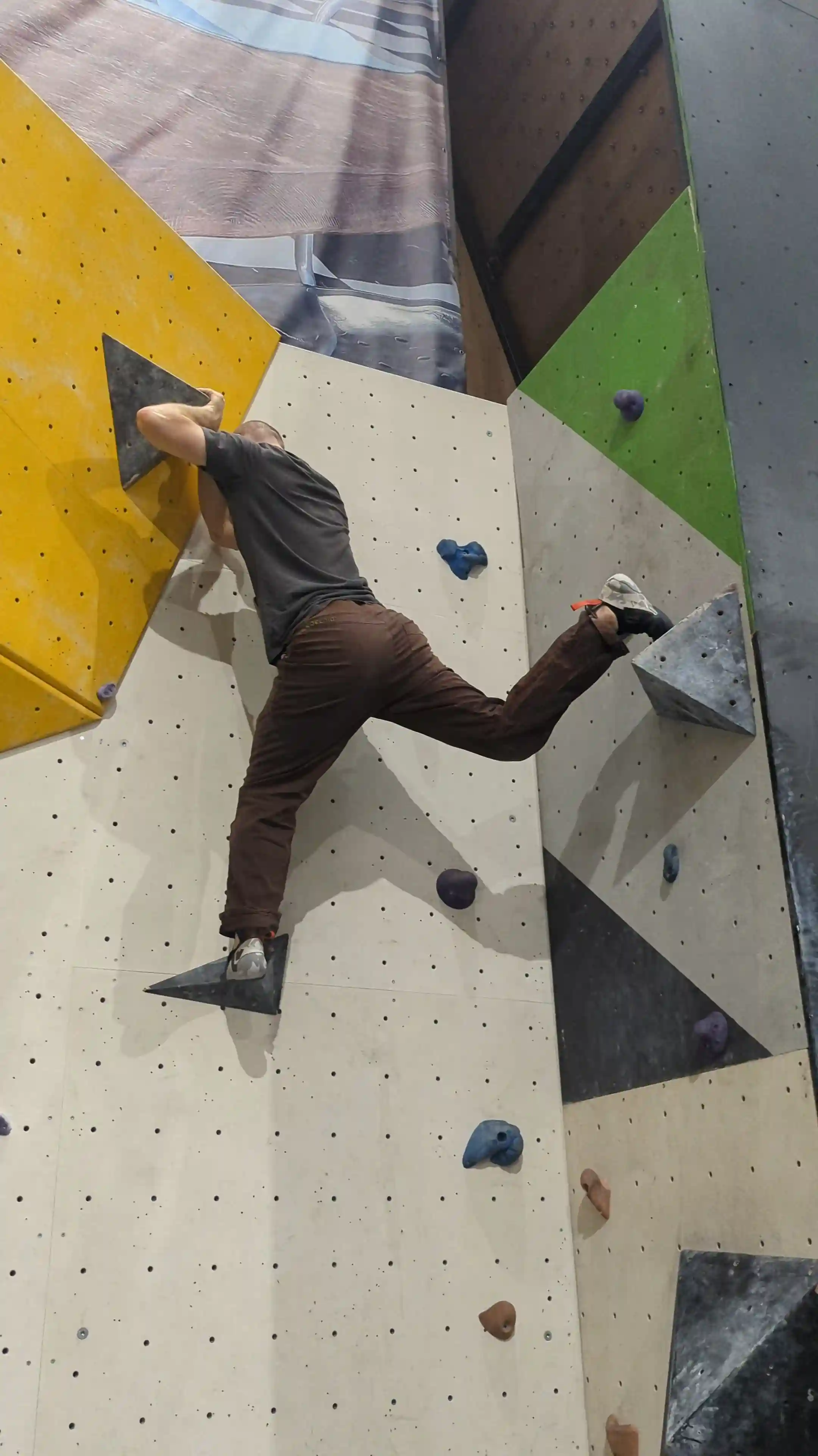 Shows the climber on the bouldering wall with both hands on the final hold after employing the knee drop technique.