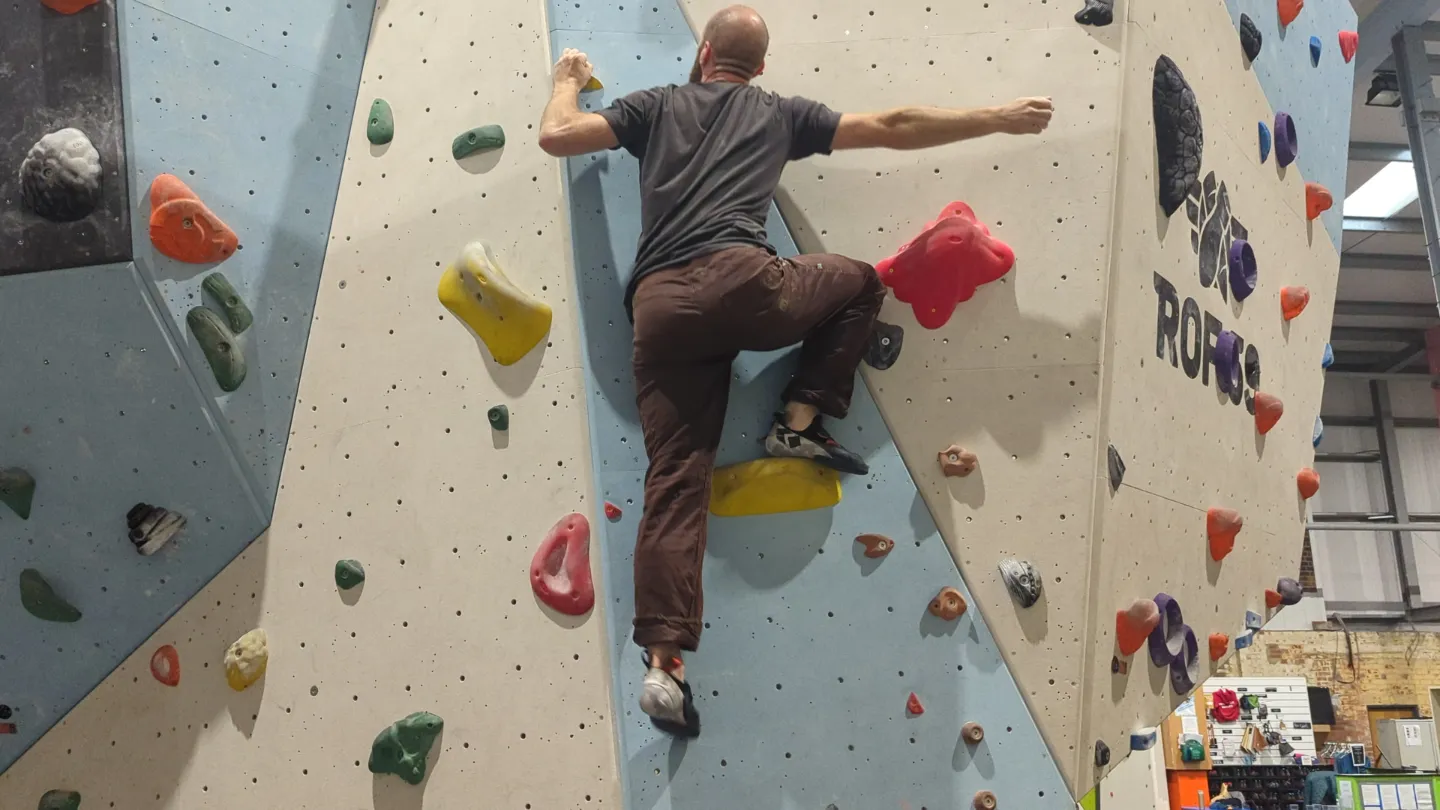 Shows the climber on the bouldering wall, pushing up from their right leg to enable themselves to climb higher.