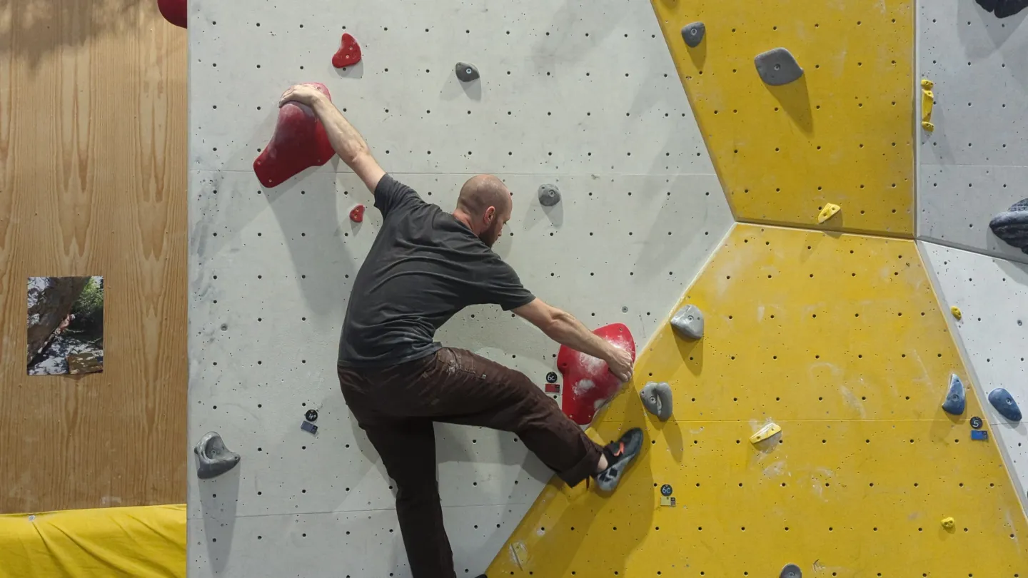 Shows the climber on the bouldering wall attempting to position his toe for the the toe hook.